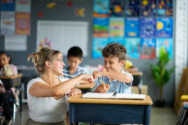 Teacher fist bumping her student at his desk